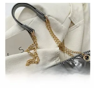 Détail de la chaîne dorée et de l'anse en cuir gris sur le sac matelassé argent