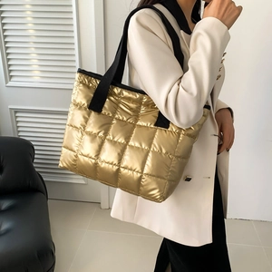 Golden quilted tote bag with black wide straps for women in a modern indoor setting
