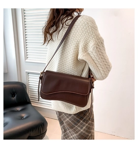 Detail of coffee brown crossbody bag with scalloped flap on model in minimalist interior