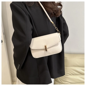 Detail of cream leather shoulder bag with gold cylindrical metal clasp and chain strap