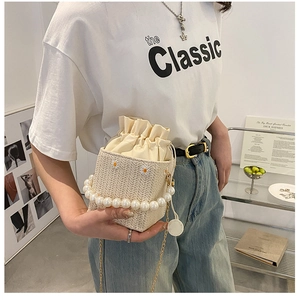 Detail of straw bucket bag featuring daisy embroidery and elegant large pearl handle