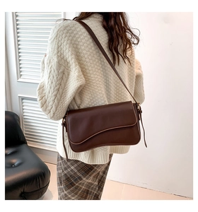 Brown leather shoulder bag with a flap cover shown on a model in a retro office setting