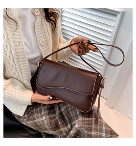 Close-up of dark brown leather shoulder bag with elegant wavy flap and gold buckle detail