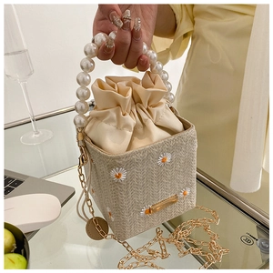 Detail of beige straw bag with daisy embroidery, pearl handle and chain strap