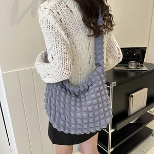 Detail view of blue textured popcorn cloud bag with a wide strap on a model's shoulder