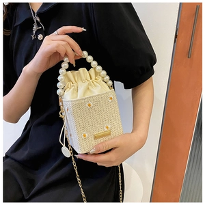 Detail of straw bucket bag featuring daisy embroidery and white pearl handle strap