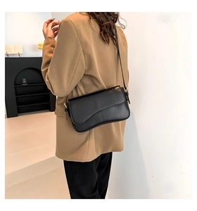 Close-up of black glossy leather crossbody bag with unique wavy flap and gold buckle
