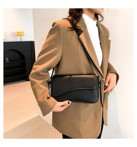 Detailed view of a black matte shoulder bag with a unique wavy flap worn with a brown blazer