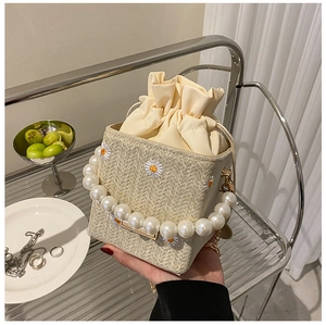 Detail of straw woven bucket bag with daisy embroidery and elegant pearl chain handle