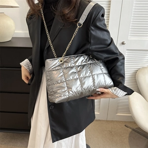 Détail d'un sac fourre-tout matelassé argenté avec chaîne dorée porté sur un blazer noir