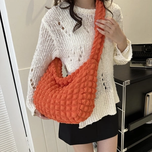 Model wearing a bright orange pleated cloud bag with a 3D bubble texture finish
