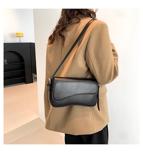 Detail view of the asymmetric saddle-style flap on the black matte leather shoulder bag