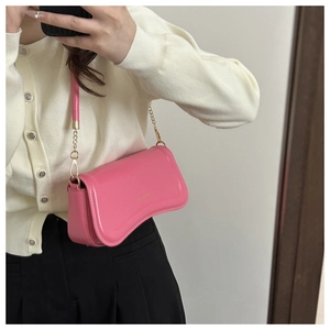 Detail of pink crescent shoulder bag with gold chain strap and metallic brand logo