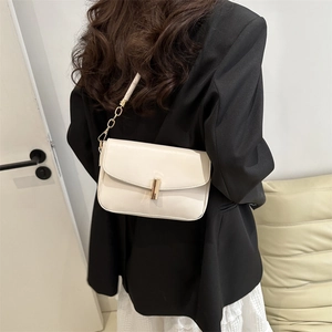 Minimalist beige crossbody bag with gold vertical clasp and elegant chain strap on model