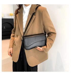 Detail of black leather shoulder bag with magnetic flap closure on a model in a blazer