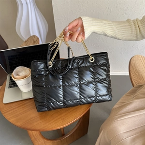 Détail d'un sac cabas noir matelassé avec grandes surpiqûres et bandoulière chaîne dorée