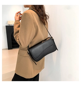 Detail of black faux leather shoulder bag with curved flap and gold metal hardware