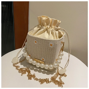 Detail of straw bucket bag featuring daisy embroidery and glossy pearl handle