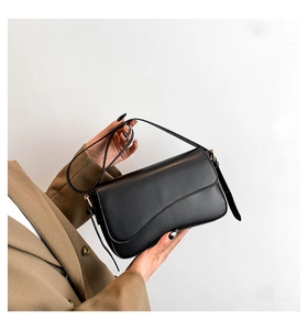 Detail of minimalist black faux leather shoulder bag with gold-tone buckle hardware