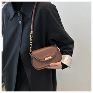 Borsa a tracolla in pelle marrone con catena dorata indossata da modella in cappotto nero