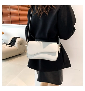 White shoulder bag with wave flap and gold hardware shown on a model in a minimalist room