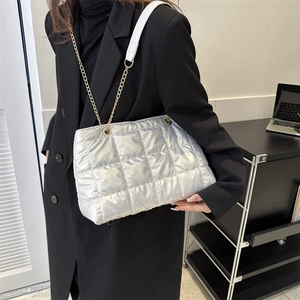 Sac à bandoulière argenté matelassé avec chaîne dorée porté par un mannequin