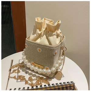 Detail of straw woven bucket bag with daisy embroidery, pearl handle and gold chain strap