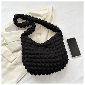 Detail of black pleated cloud bag with bubble texture shown on a beige blazer background