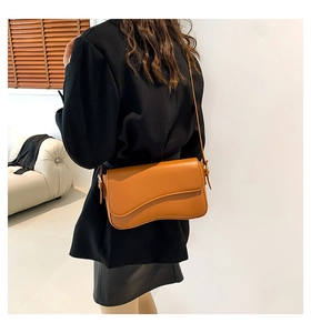 Detail of caramel shoulder bag featuring a wavy flap design and slim leather strap