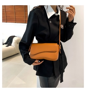 Detail of the asymmetric wave-shaped flap on the orange-brown leather shoulder bag