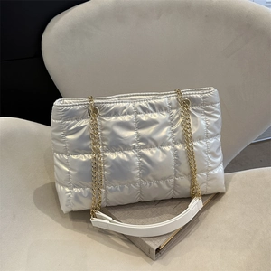 Détail d'un sac cabas argenté matelassé avec des bandoulières en chaîne dorée sur sofa