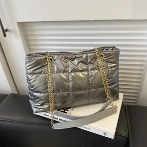 Détail du sac bandoulière argenté métallisé avec chaînes dorées sur surface blanche