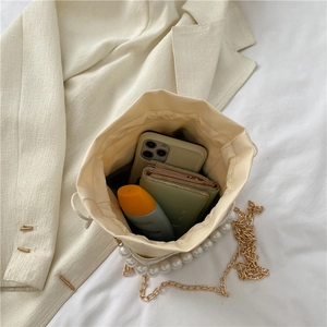 Cream drawstring bucket bag with pearl accents and gold chain strap on white bedding