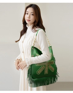 Detail of green leather shoulder bag with gold square studs, fringe, and metal chain strap