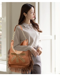 Detail of tan shoulder bag featuring punk studs, long tassels, and gold chain strap
