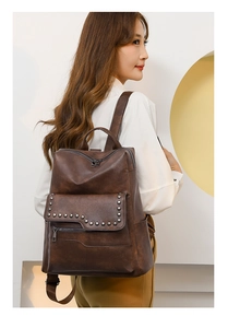 Detail of dark brown leather backpack featuring silver rivets and adjustable straps on model