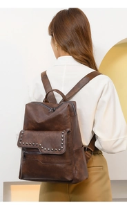 Rear view of model wearing a vintage brown faux leather backpack with metallic rivets