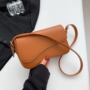 Brown leather crossbody shoulder bag with asymmetric flap on office desk background