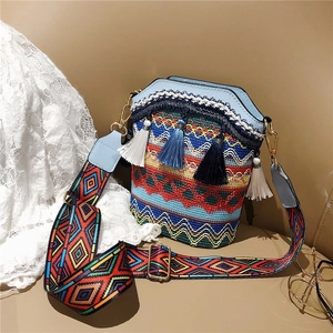 Ethnic woven bucket bag with tassels and colorful wide strap on beige background