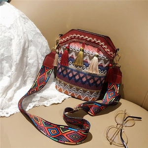 Bohemian woven bucket bag with colorful tassels and patterned crossbody strap on a desk