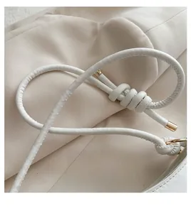 Detail of a white leather handbag featuring a unique knotted handle and gold metal accents