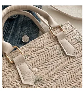 Détail du sac à main en paille avec anse en cuir beige et boucle dorée en D