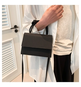 Detail of black woven texture crossbody bag with knot handle worn by a model