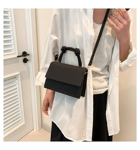 Detail of black woven texture crossbody bag featuring a unique knotted handle design
