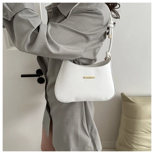 Detail view of a white shoulder bag with gold metal trim styled with a grey shirt