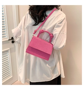 Detail of woven pink crossbody bag with knotted handles worn by a model in a white shirt