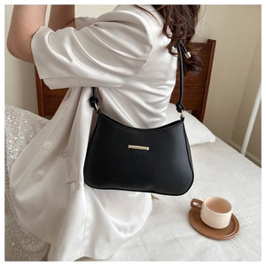 Detail of a black half-moon shoulder bag with a gold metal bar on a white blazer