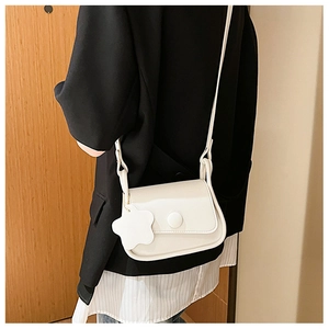 Dettaglio di una borsa a tracolla bianca minimalista con ciondolo a fiore e chiusura