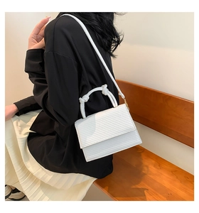 White woven texture crossbody bag with unique knot handle shown in a lifestyle street setting