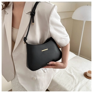 Detail of a matte black leather shoulder bag with gold hardware and knotted strap on a model